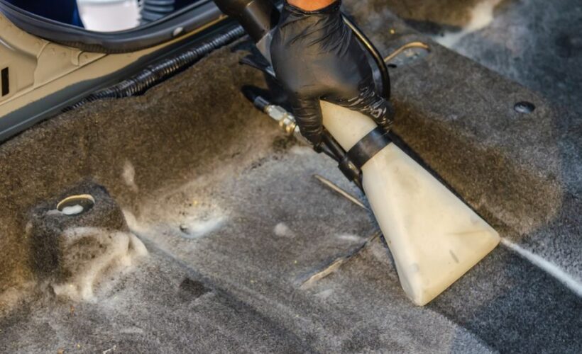 A hand in a glove using a vacuum to clean a car interior carpet, removing dirt effectively. - Photo by Khunkorn Laowisit on Pexels
