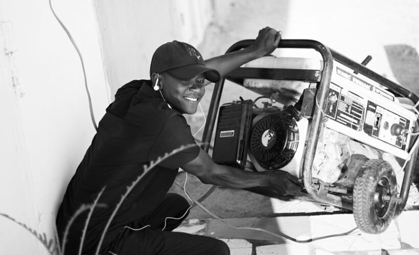 A cheerful young man wearing a cap and earphones operating a portable generator outside. - Photo by Abdulkadir muhammad sani on Pexels