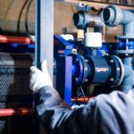 A worker in blue sleeves inspects machinery pipes and equipment at an industrial plant. - Photo by cang hai on Pexels