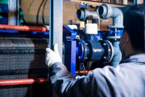 A worker in blue sleeves inspects machinery pipes and equipment at an industrial plant. - Photo by cang hai on Pexels