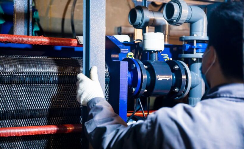 A worker in blue sleeves inspects machinery pipes and equipment at an industrial plant. - Photo by cang hai on Pexels
